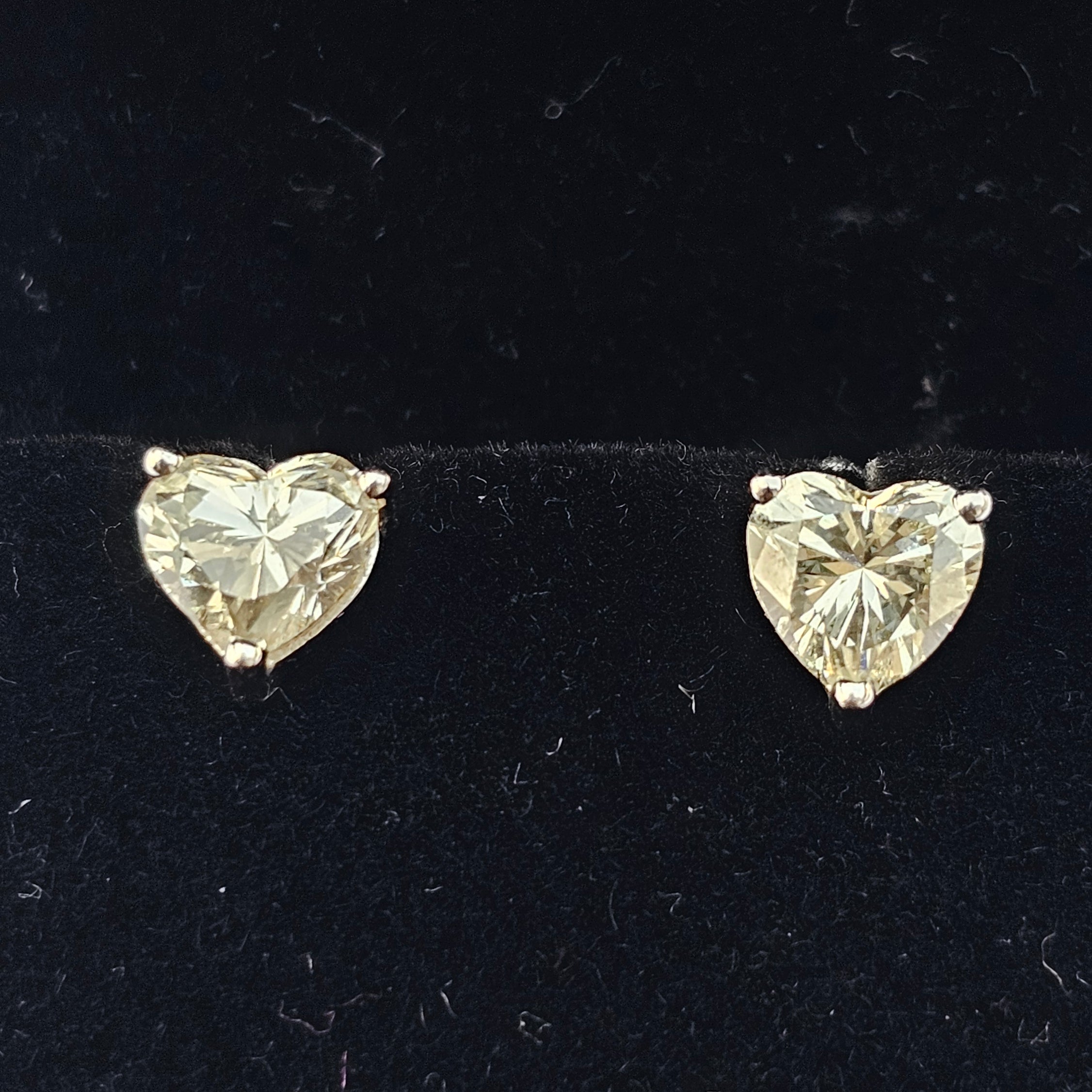 Two heart-shaped diamond earrings on a black background