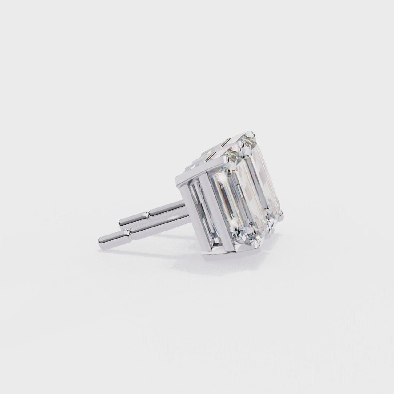 Pair of emerald-cut diamonds with gold prongs on a white background