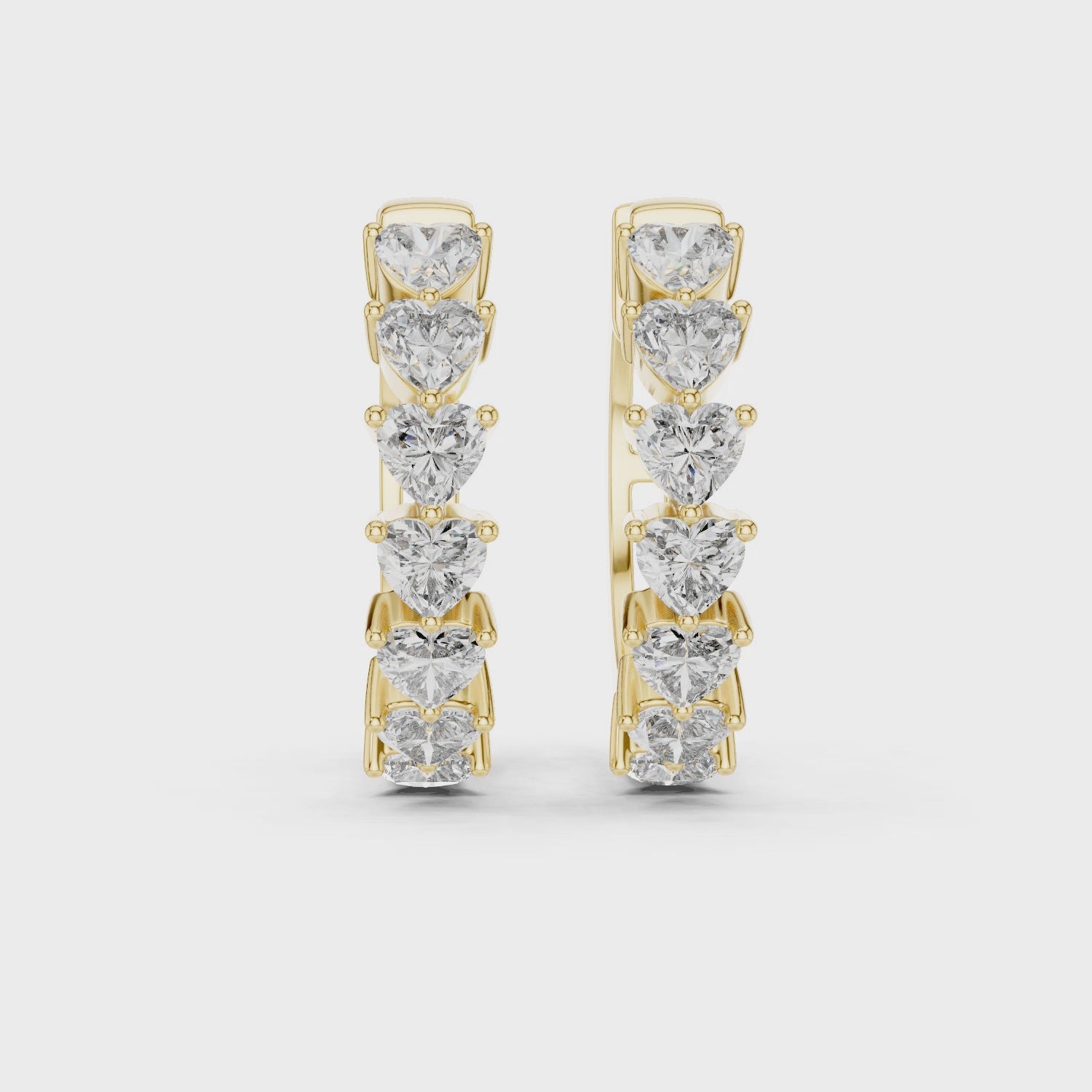 Pair of gold hoop earrings with heart-shaped diamonds on a white background